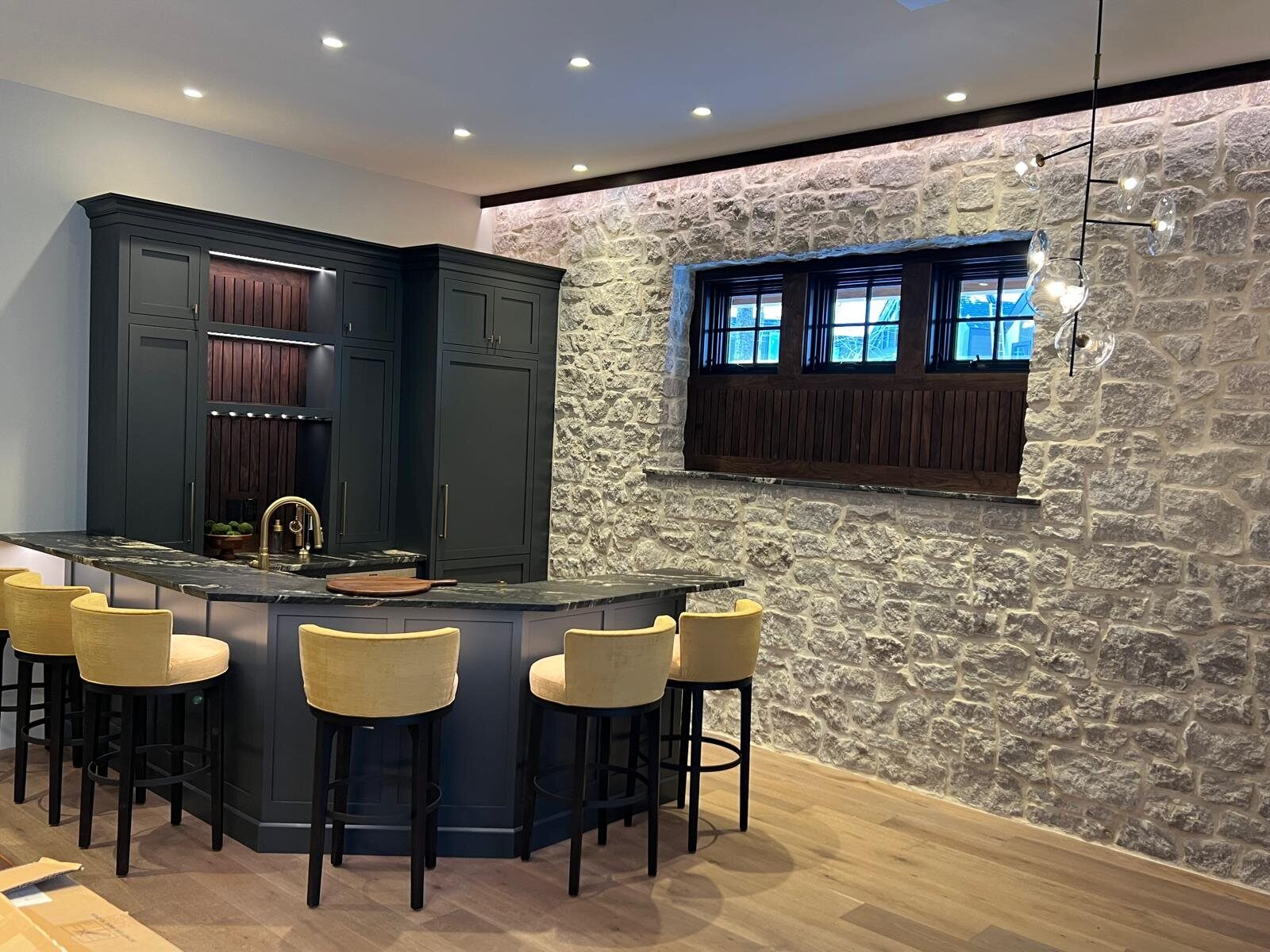 Custom bar cabinetry in dark green set against a natural stone wall