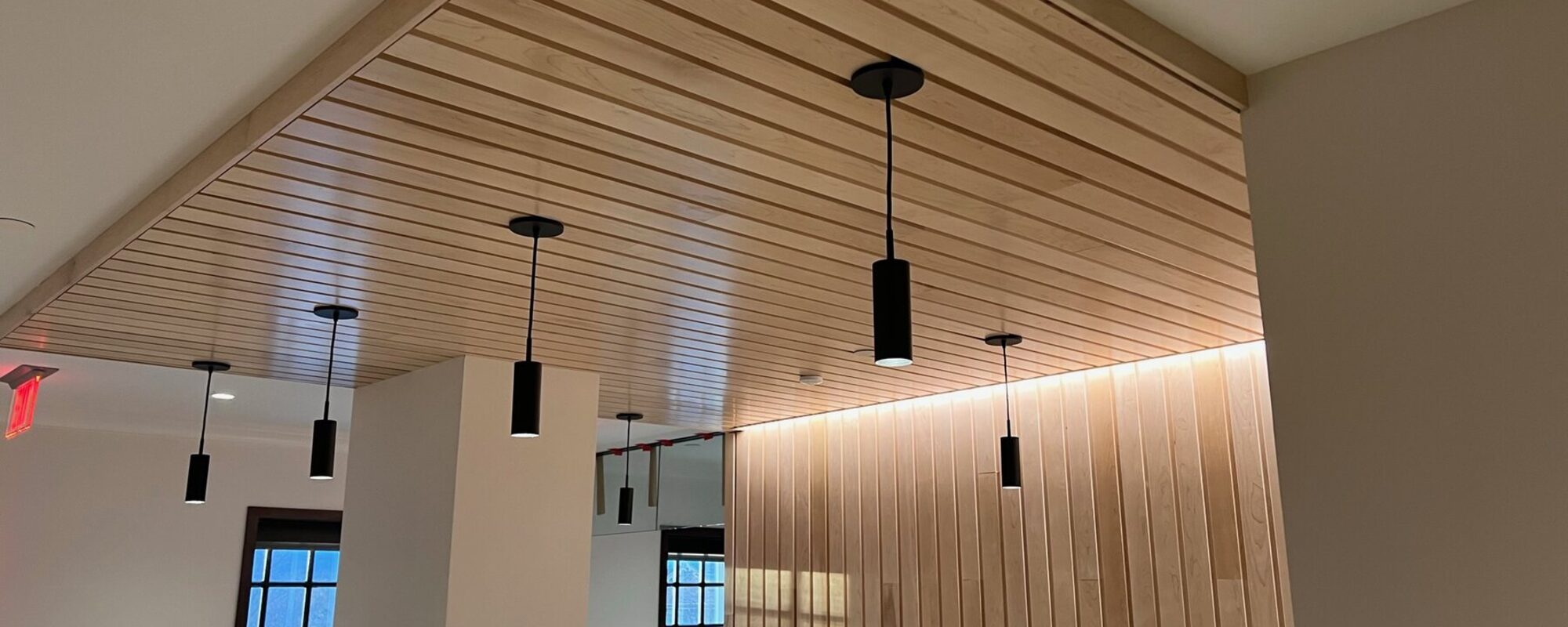 Wood plank ceiling with pendant lighting over a bright open space