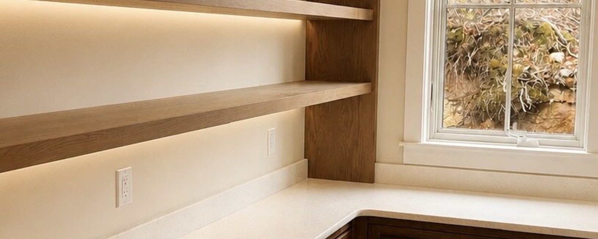Custom floating shelves over built-in wood drawers beside a window