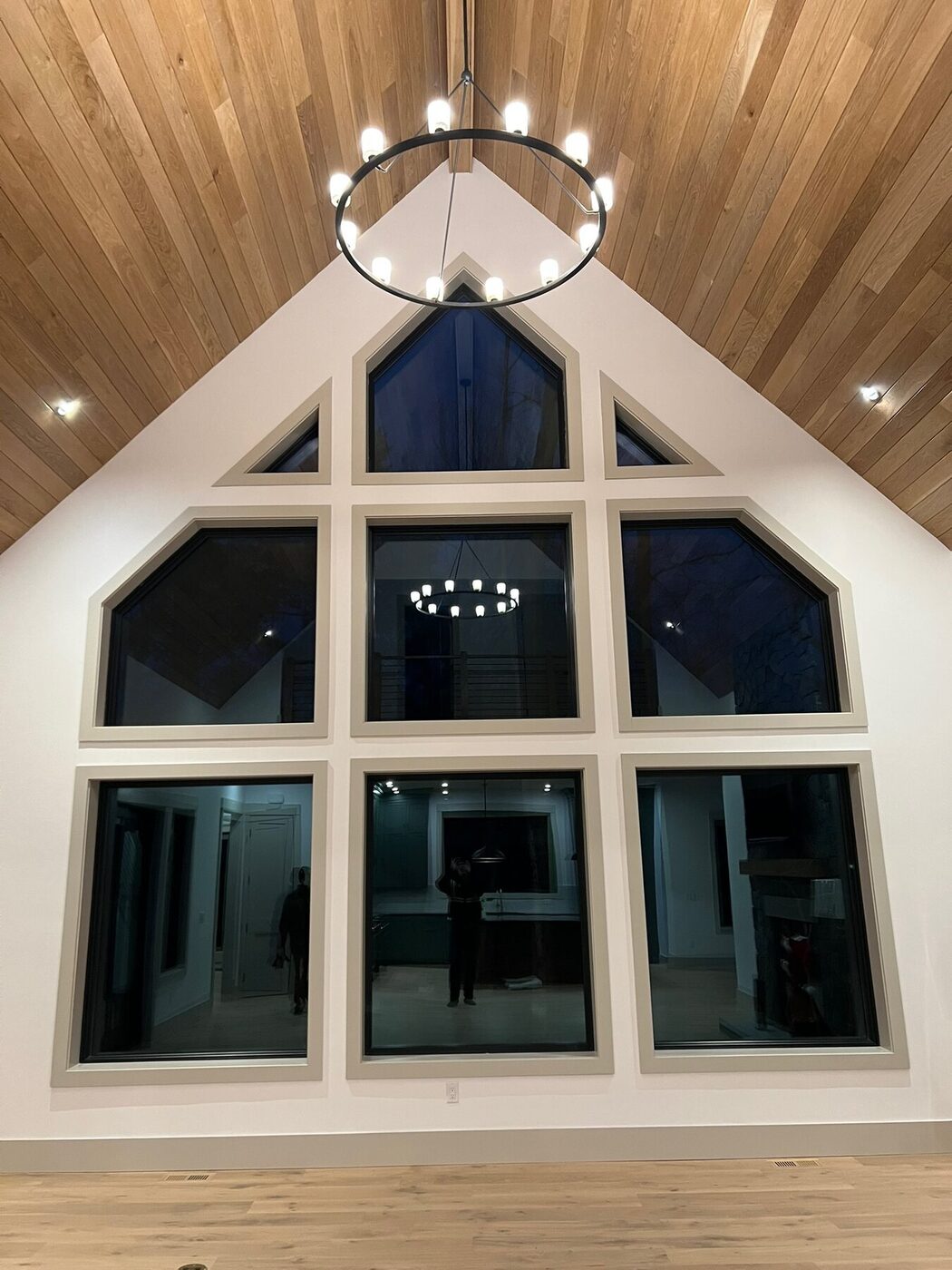 Wood plank cathedral ceiling with a chandelier above a custom trimmed window wall