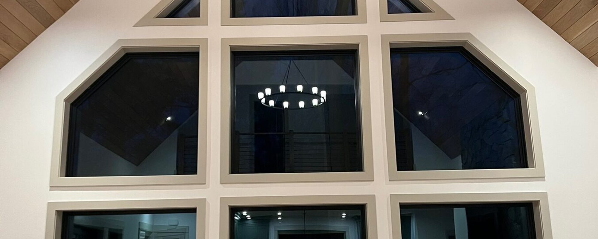 Wood plank cathedral ceiling with a chandelier above a custom trimmed window wall