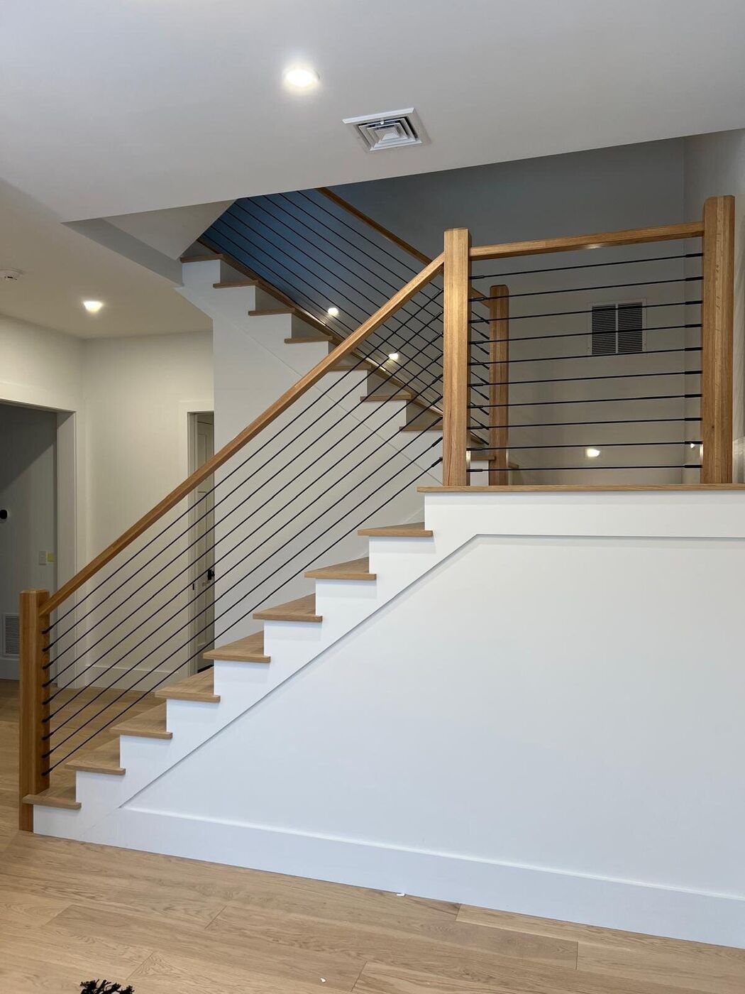 Staircase with a wood handrail and horizontal cable railing